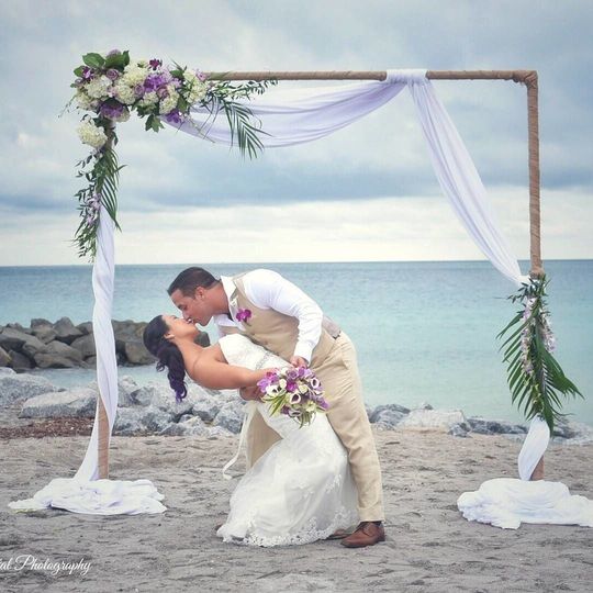 bride and groom kissing under arch at beach