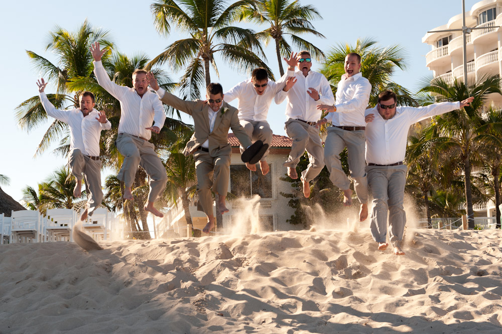 groom and groomsmen jumping in sand on the beach