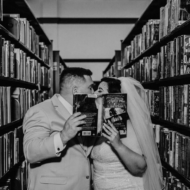bride and groom kissing behind book in library